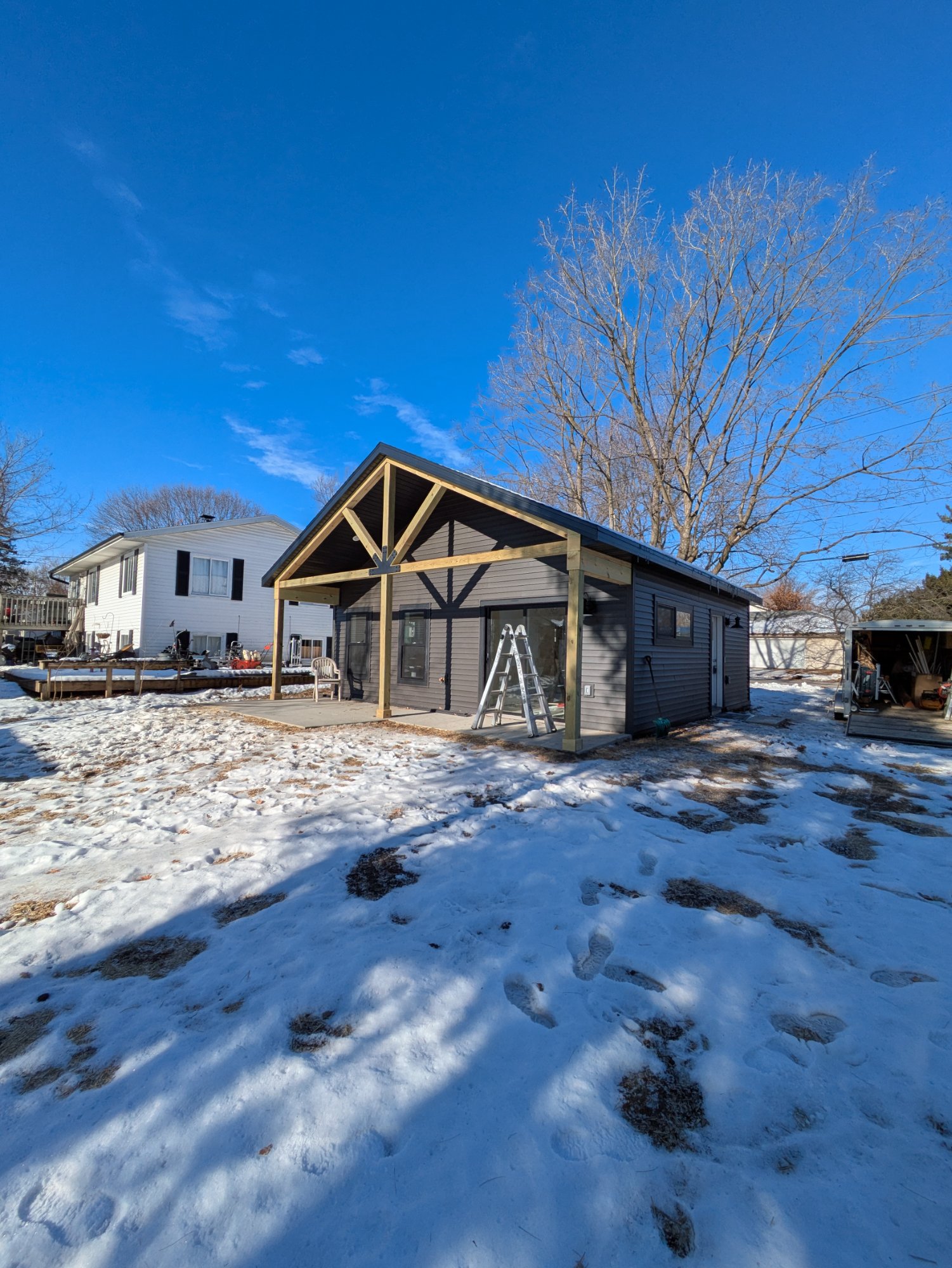 Finished ADU exterior in winter — dark siding, timber porch, blue sky — North Side Madison WI, December 2025