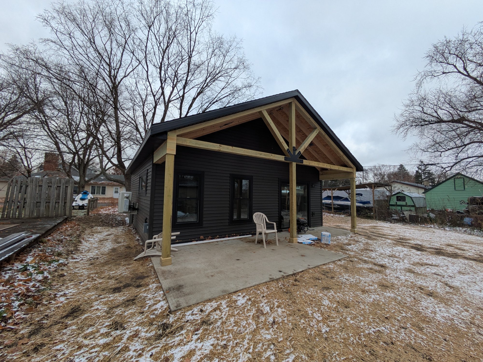 Near-complete ADU exterior with first snow — dark siding, gable porch — North Side Madison WI